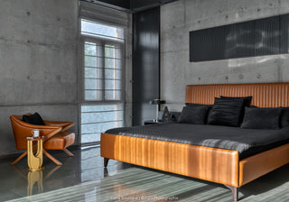 Modern bedroom with a brown leather bed and armchair against a concrete wall.