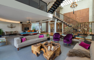 Modern living room with a staircase, gray sofa, purple chairs, and wooden coffee table.