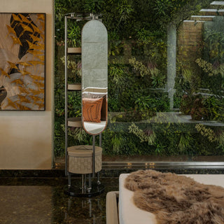 Decorative standing mirror with a cushion against a wall with greenery