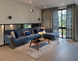 Modern living room with a blue sofa, wooden coffee table, and large windows.