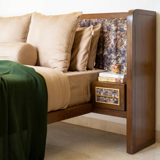 Bed with wooden backrest and a small table with decorative items.