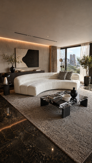 Modern living room with a curved white sofa, coffee table, and city view.