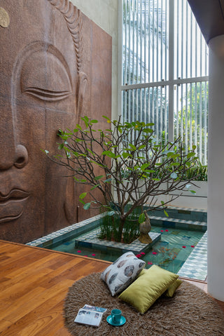 Indoor setting with a large stone sculpture, potted plant, and cushions on a wooden floor.